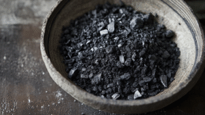 A ceramic bowl filled with coarse, black charcoal pieces sits on a rustic wooden surface, reminding you to Safely Dispose of Hot Coals after use.
