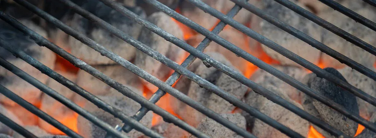 Close-up of a barbecue grill grate positioned over hot, glowing charcoal briquettes—perfect for following tips from our Grill Thermometers Guide.
