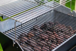 Close-up of an empty metal charcoal grill with two grates, showing unlit lava rocks beneath the lower grate—similar to those used when asking, "Do propane BBQ need briquettes?.