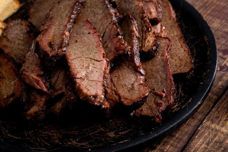 Several slices of smoked brisket are arranged on a dark plate, showing a dark bark on the edges and a tender, juicy interior—a true showcase for expert seasoning tips.